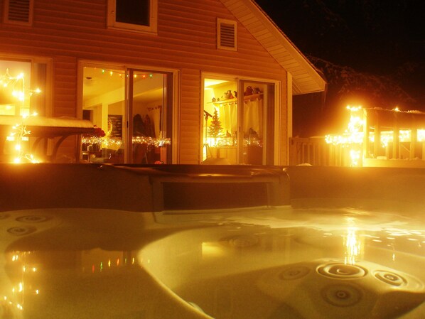 A hot tub area with a wooden deck and a house in the background.