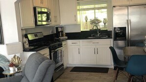 A modern kitchen with white cabinets, stainless steel appliances, and a dining area with blue chairs. - Beach house on the beach! (Ventura)