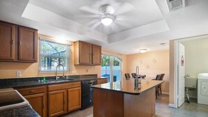 Une cuisine avec des meubles de rangement en bois, un plan de travail noir, un îlot central et un ventilateur de plafond.