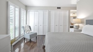 A bedroom with a large bed, a chair, a nightstand with a lamp, and white closets. - Renovated, Ground Level, 2 BR 2 BA, WiFi, Cable, Pool. 4 individuals max. (Pinehurst)