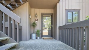 A building entrance with a number '130' sign, a door, a small potted plant, and a metal trash can. - Renovated, Ground Level, 2 BR 2 BA, WiFi, Cable, Pool. 4 individuals max. (Pinehurst)