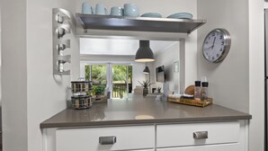 A modern kitchen with a stainless steel range hood, a wall-mounted clock, and a window overlooking a garden. - Renovated, Ground Level, 2 BR 2 BA, WiFi, Cable, Pool. 4 individuals max. (Pinehurst)