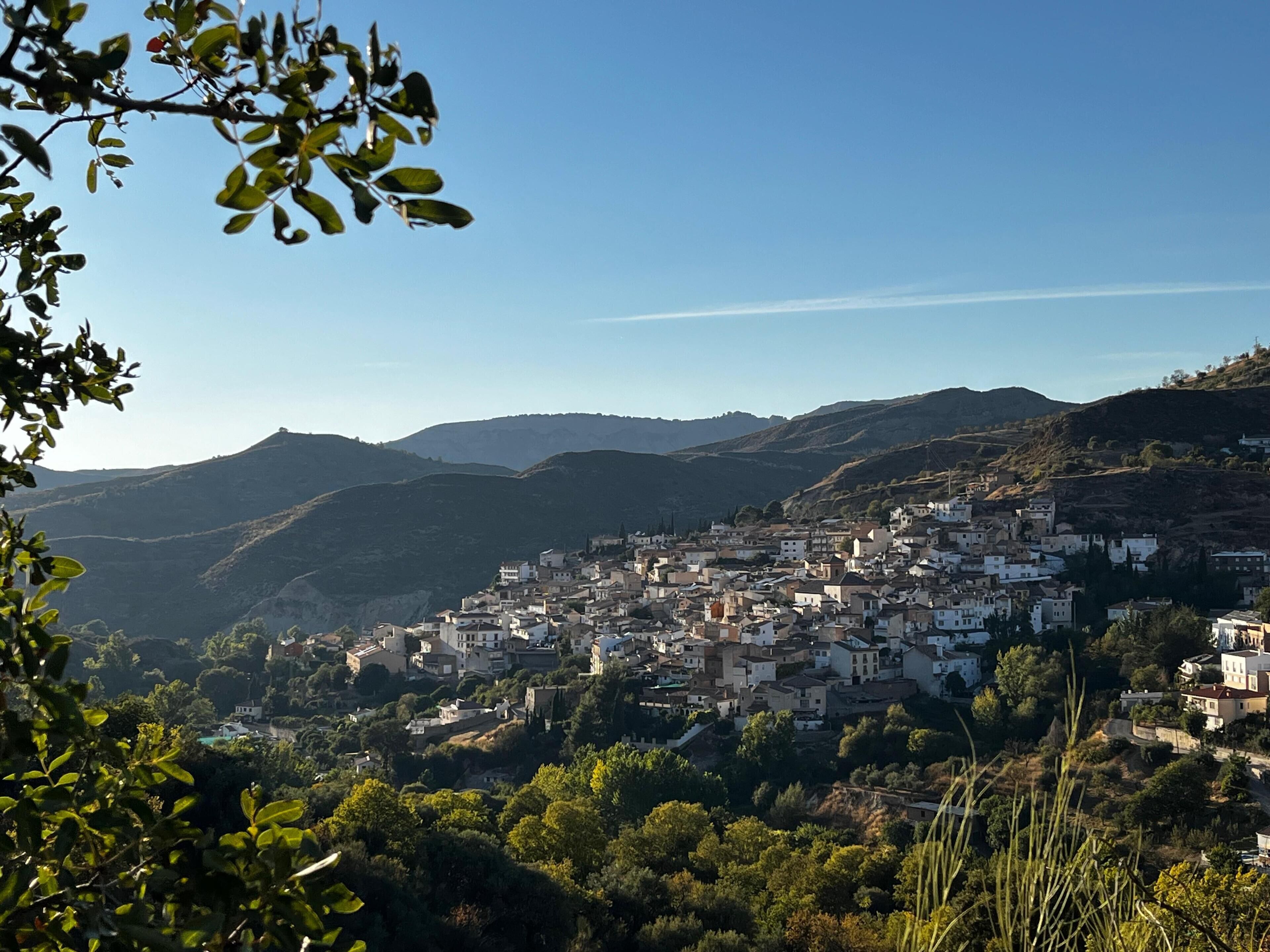 Un pueblo en la ladera de una colina con construcciones muy juntas, rodeado de colinas y vegetación.