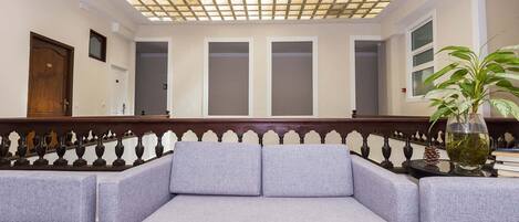 A room with a grey sofa, a wooden railing, and a ceiling with a grid pattern.