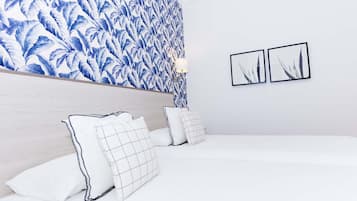 Een slaapkamer met een bed, kussens, een hoofdeinde en een muur met een blauw bladpatroon. Er hangen twee ingelijste foto's aan de muur.