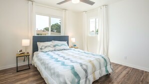 Ein Schlafzimmer mit einem Bett, zwei Nachttischen, einem Deckenventilator und einem Fenster mit Vorhängen.