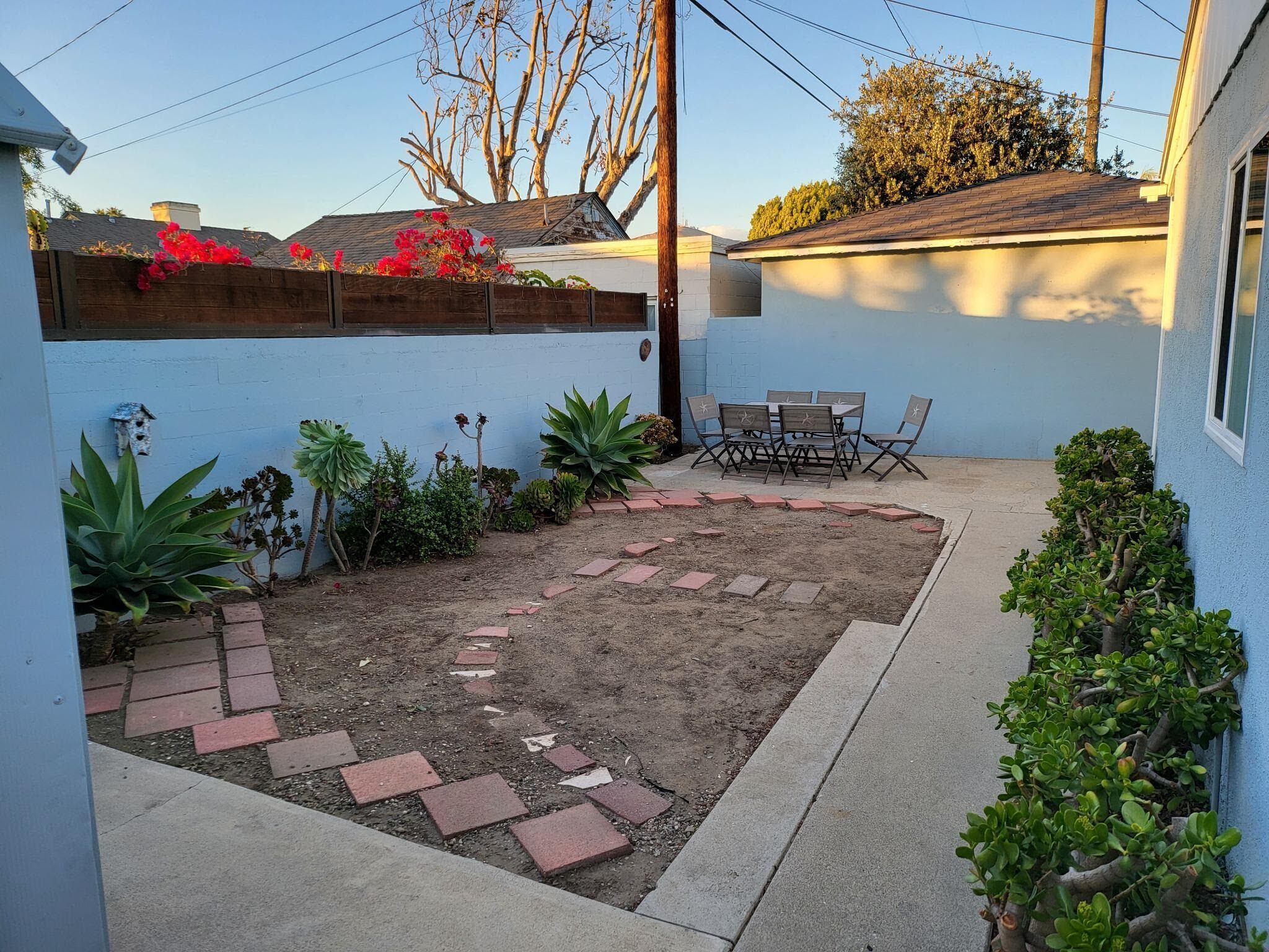 A backyard with a patio, a small table and chairs, and various plants.