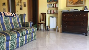 A living room with a patterned sofa, a wooden cabinet, a bookshelf, and a radiator. - Casa Flavia (Santa Flavia)