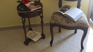 A chair with a floral cushion and a book on it, a small table with a red flower and a book, and a wall with a floral pattern. - Casa Flavia (Santa Flavia)