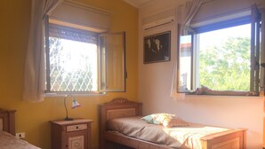 A bedroom with two wooden beds, a nightstand with a lamp, and a window with curtains. - Casa Flavia (Santa Flavia)