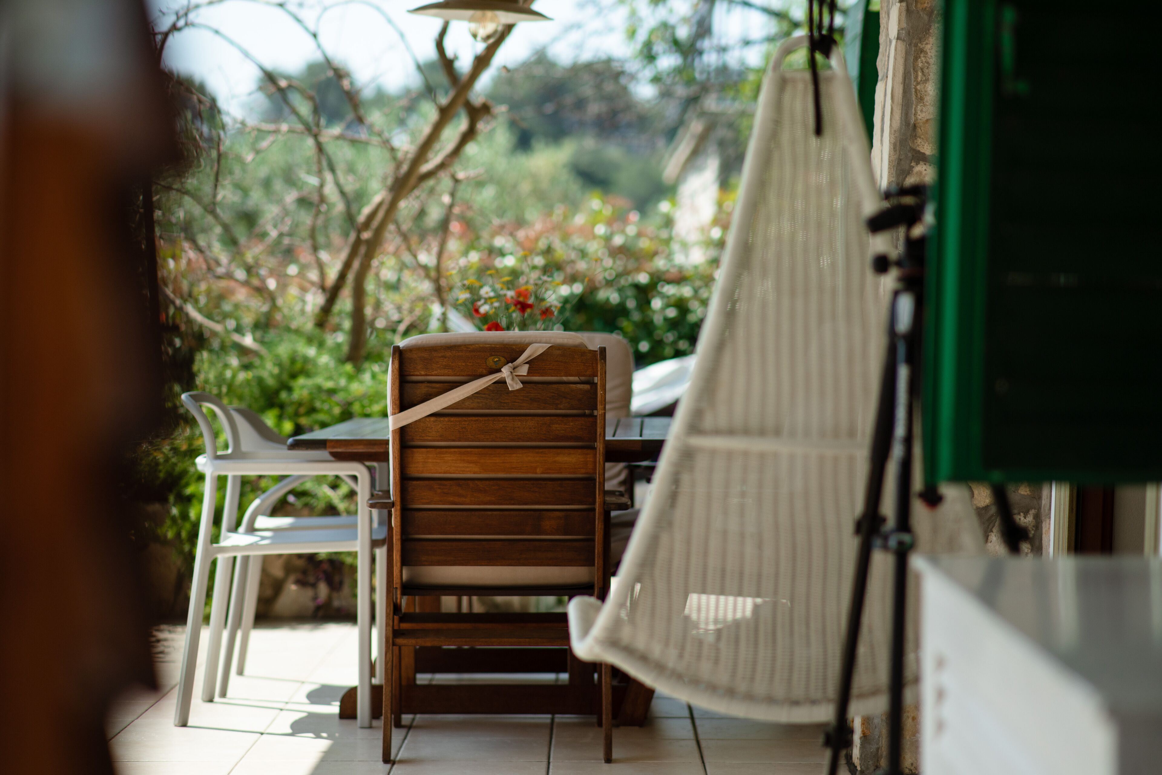 Une chaise en bois avec un coussin, une chaise blanche et une chaise suspendue dans une pièce donnant sur un jardin.