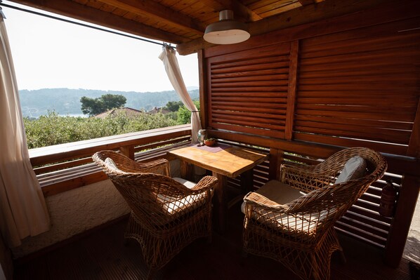 A wooden balcony with wicker chairs and a table, overlooking a scenic landscape.