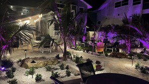 Espaço ao ar livre bem iluminado com assentos e plantas, rodeado por edifícios com janelas iluminadas.