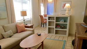 A living room with a sofa, a coffee table, a bookshelf, and a chair. - Bayfront 2 Bedroom with Private Dock and Beach Access Riley's Retreat (Treasure Island)