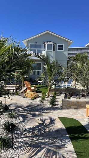 Uma casa moderna de dois andares com varanda, cercada por plantas tropicais e um espaço de lazer com piso.