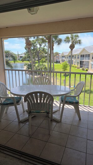 A balcony with a table and chairs, overlooking a body of water and a well-maintained lawn with palm trees.