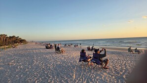 A beach with people sitting on chairs and blankets, a clear sky, and palm trees. - 300 OFF APRIL TO NOVEMBER (Naples)