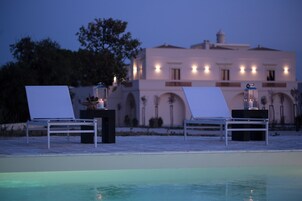 Uma área à beira da piscina com duas espreguiçadeiras e uma mesa, cada uma com uma vela e um candeeiro.