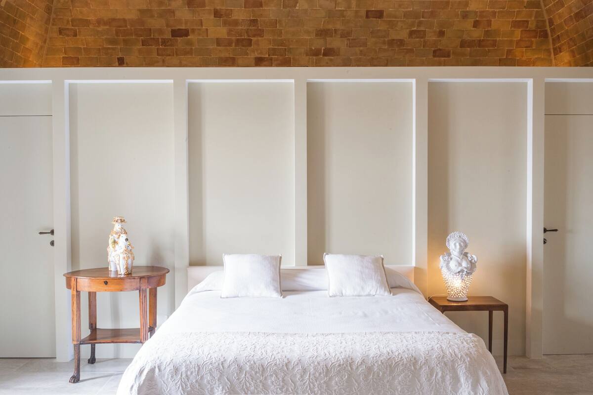 Een slaapkamer met een groot bed, een klein houten nachtkastje en een decoratief buste op het nachtkastje.