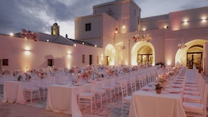 Una sala da banchetto con tavoli apparecchiati per un evento formale, con tovaglie bianche e composizioni floreali al centro.