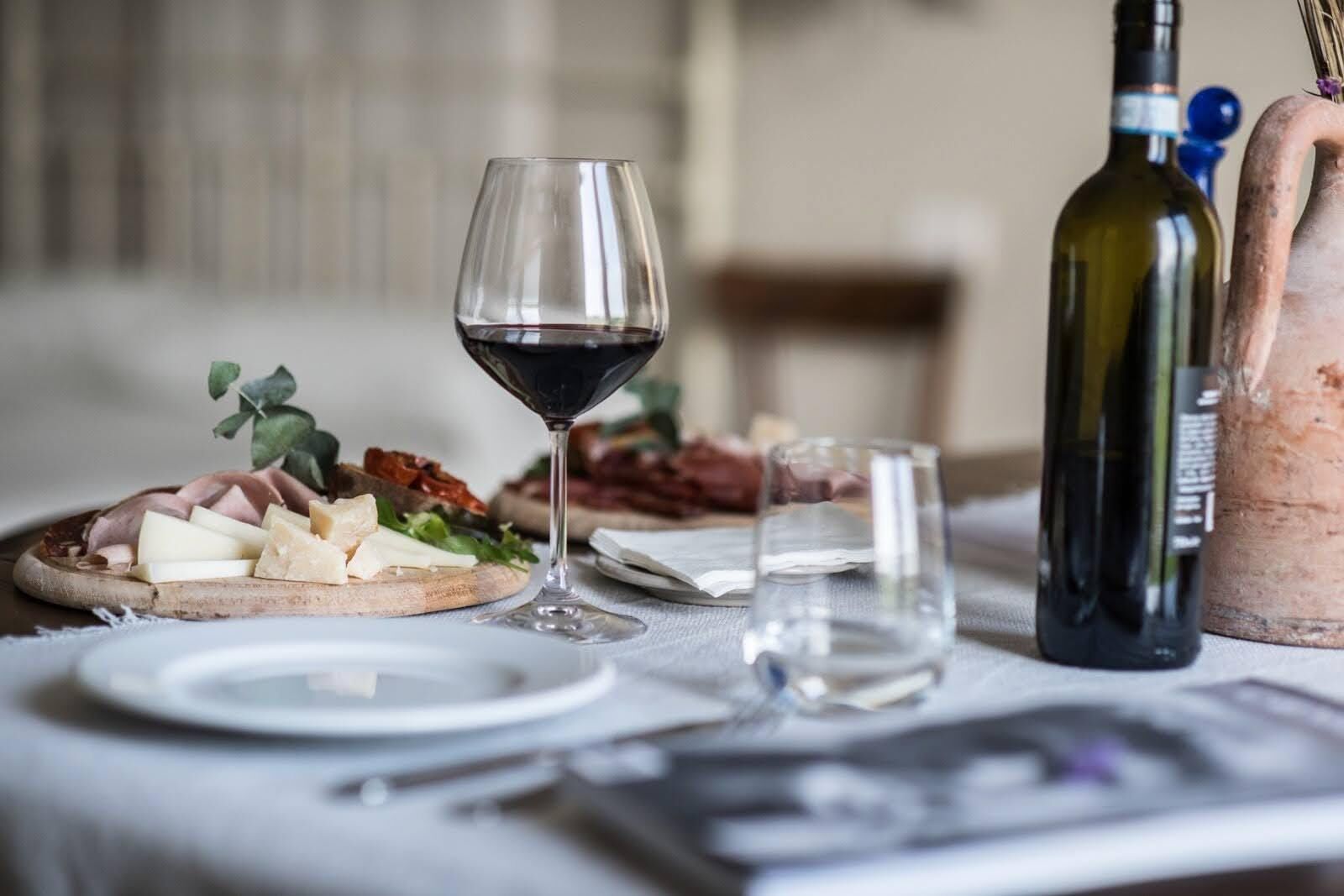 A table set with a wine glass, cheese platter, and bottles of wine.
