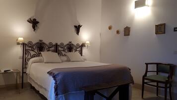 Una cama bien hecha con un edredón a rayas, una mesita de noche de madera, una silla y lámparas fijadas a la pared.