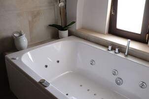A modern bathroom with a large white bathtub, a small potted plant, and a window with a view.