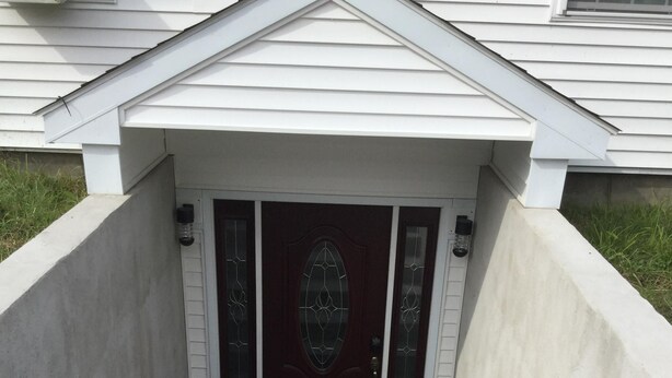 A front view of a house with a dark wooden door, white siding, and a concrete front porch leading to a set of stairs. - comfort, luxury, privacy (Amherst)