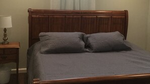 A bed with a wooden headboard, two pillows, a bedside table with a lamp, and a trash bin. - comfort, luxury, privacy (Amherst)