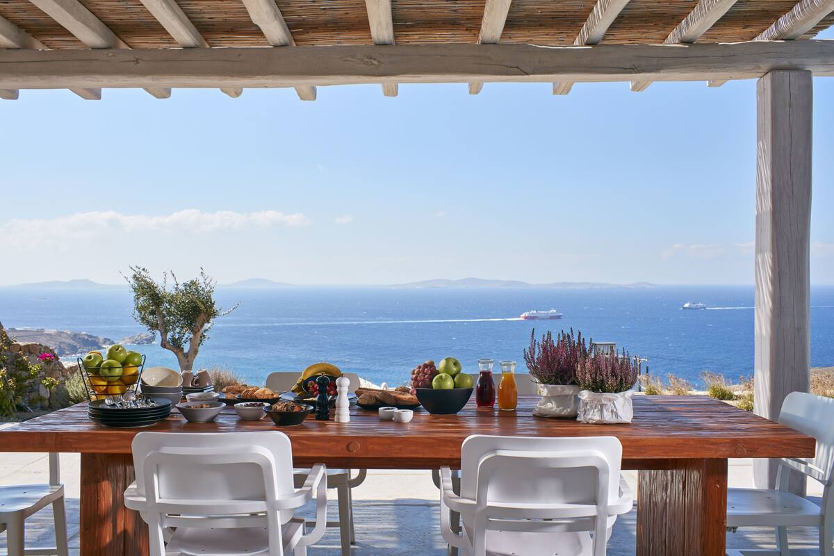 Una mesa de madera servida con alimentos para el desayuno y vista al mar.