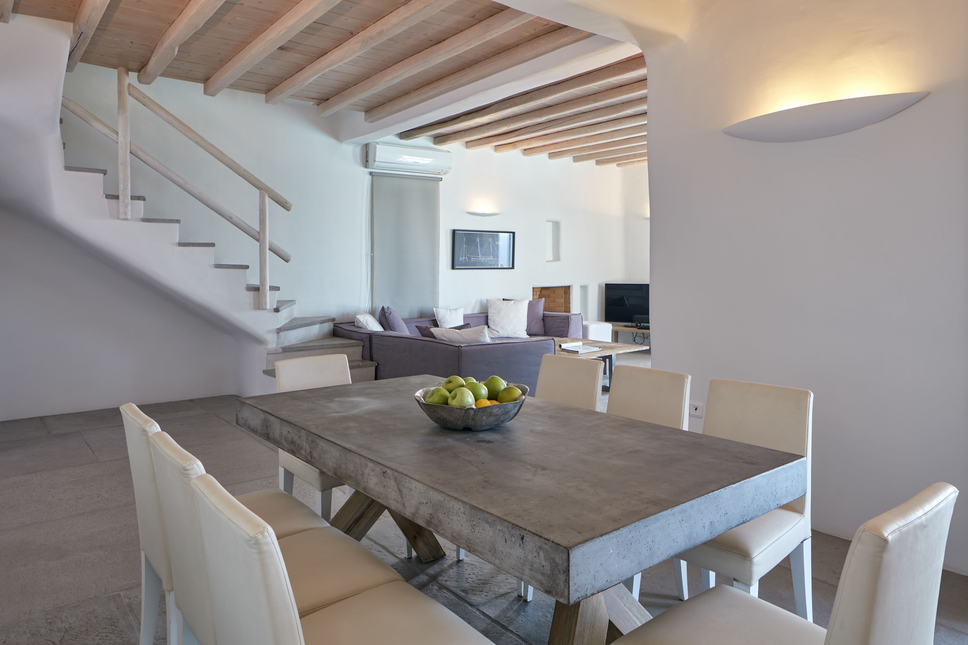 Un comedor moderno con una mesa de hormigón, sillas blancas y un cuenco de fruta.