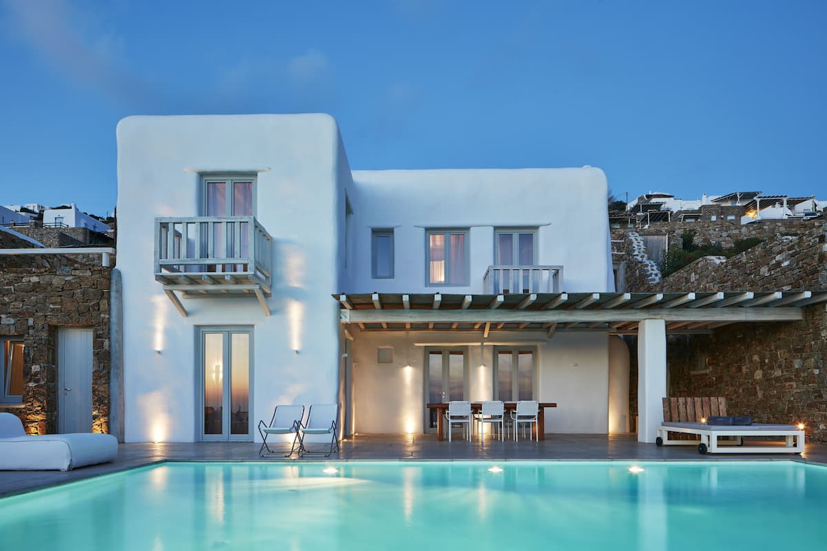 Una villa moderna con piscina, mobiliario exterior y un muro de piedra.