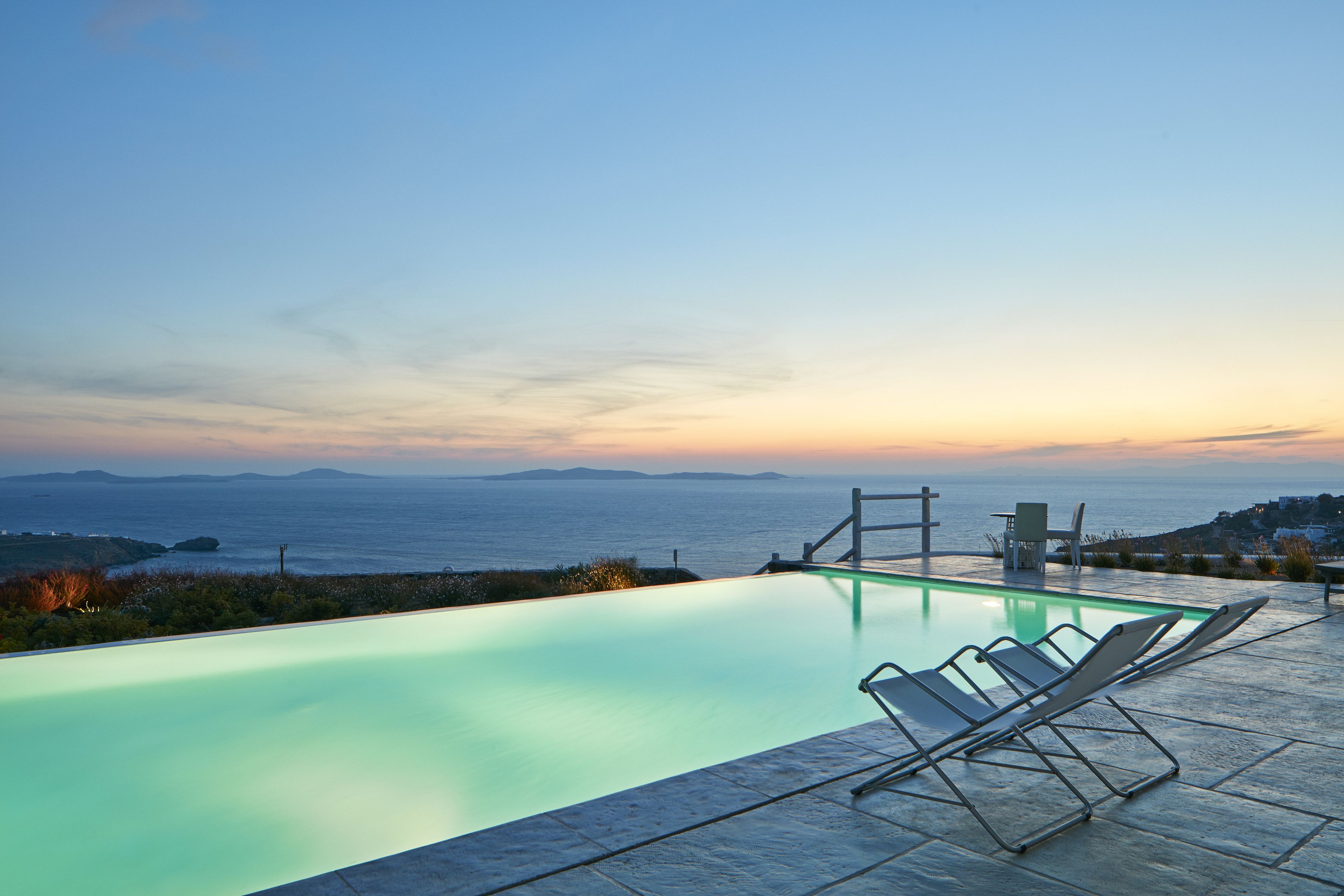A swimming pool with a view of the sea and distant mountains at sunset.