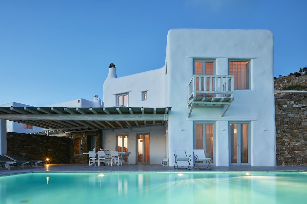 Un edificio moderno blanco con piscina, mobiliario exterior y una pared de piedra.