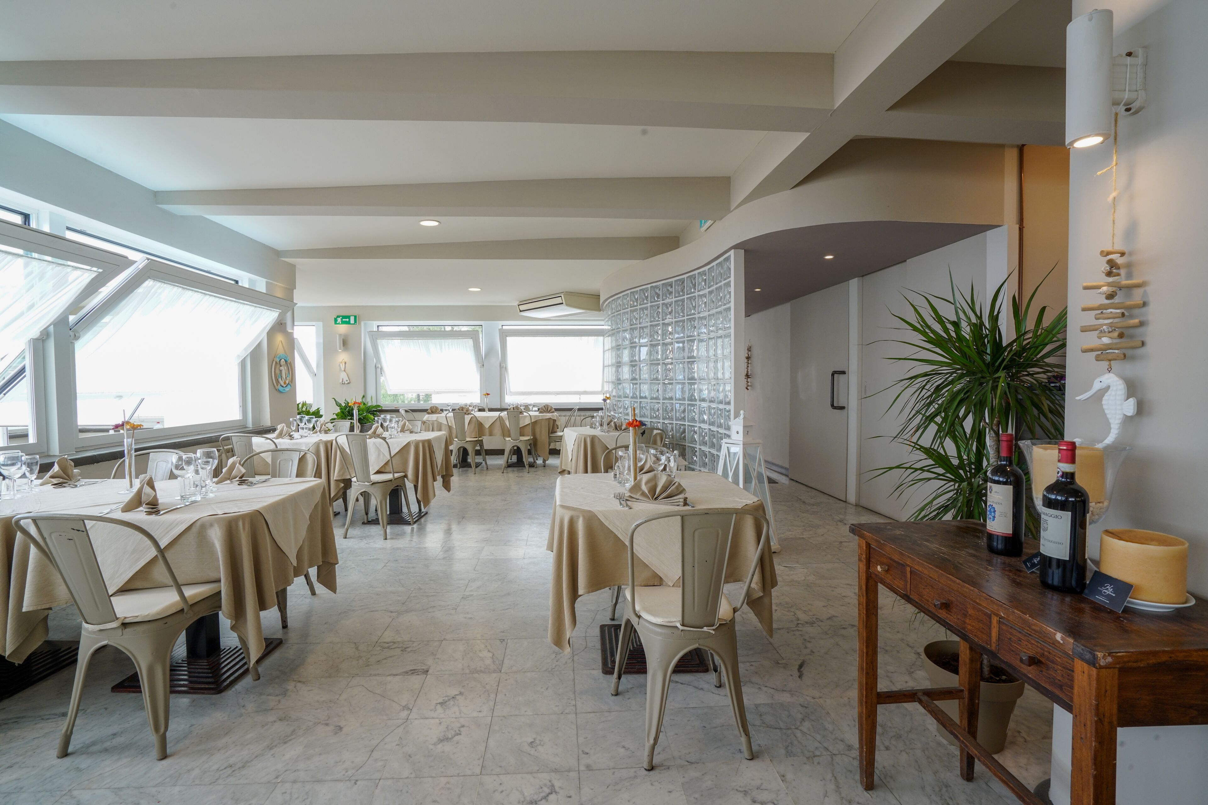 Un comedor amplio con varias mesas dispuestas para una comida, una pared decorativa y una planta a la derecha.
