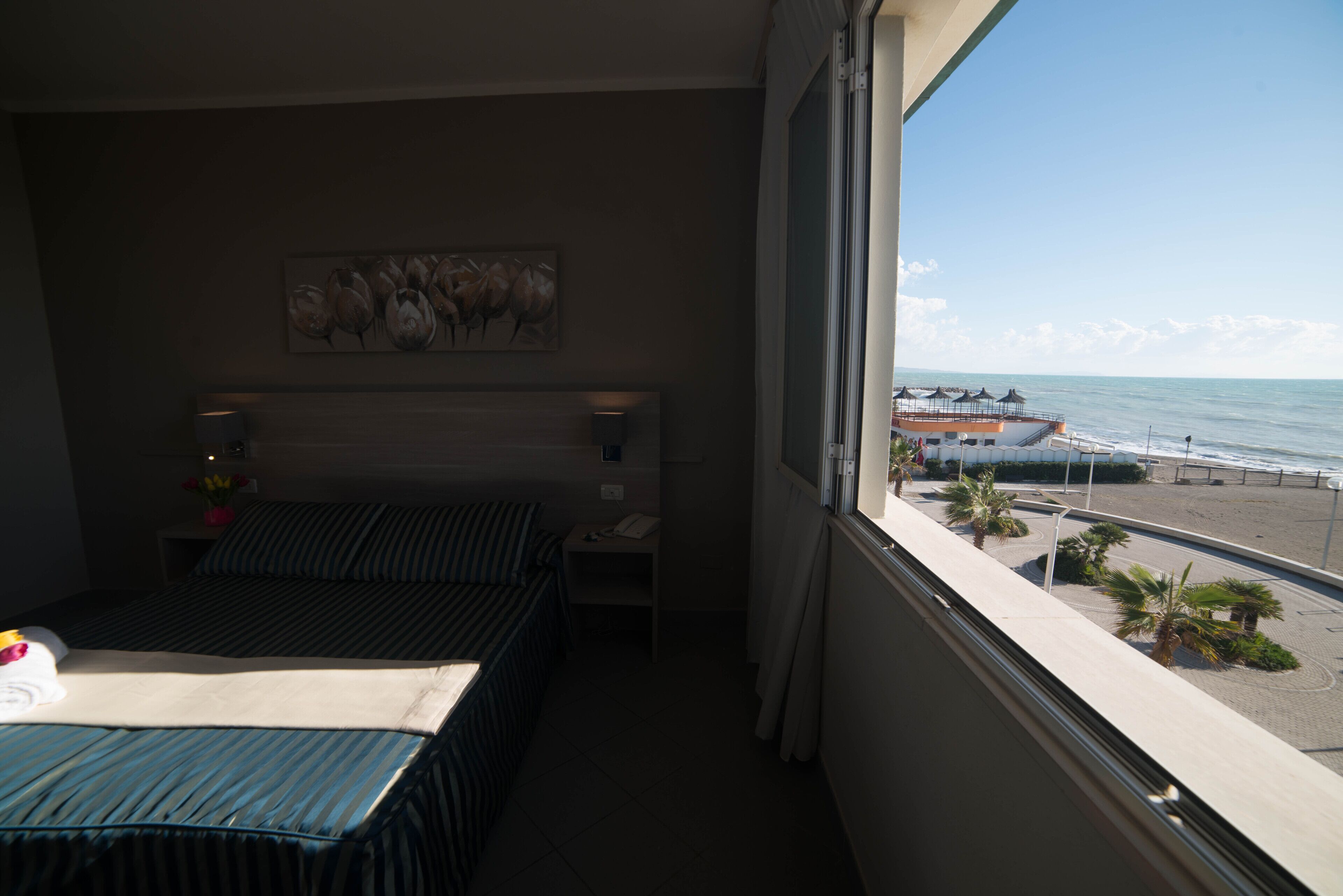 Una habitación de hotel con cama, mesita de noche, un cuadro y vistas a la playa y al océano.