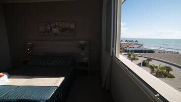 Una habitación de hotel con cama, mesita de noche, un cuadro y vistas a la playa y al océano.