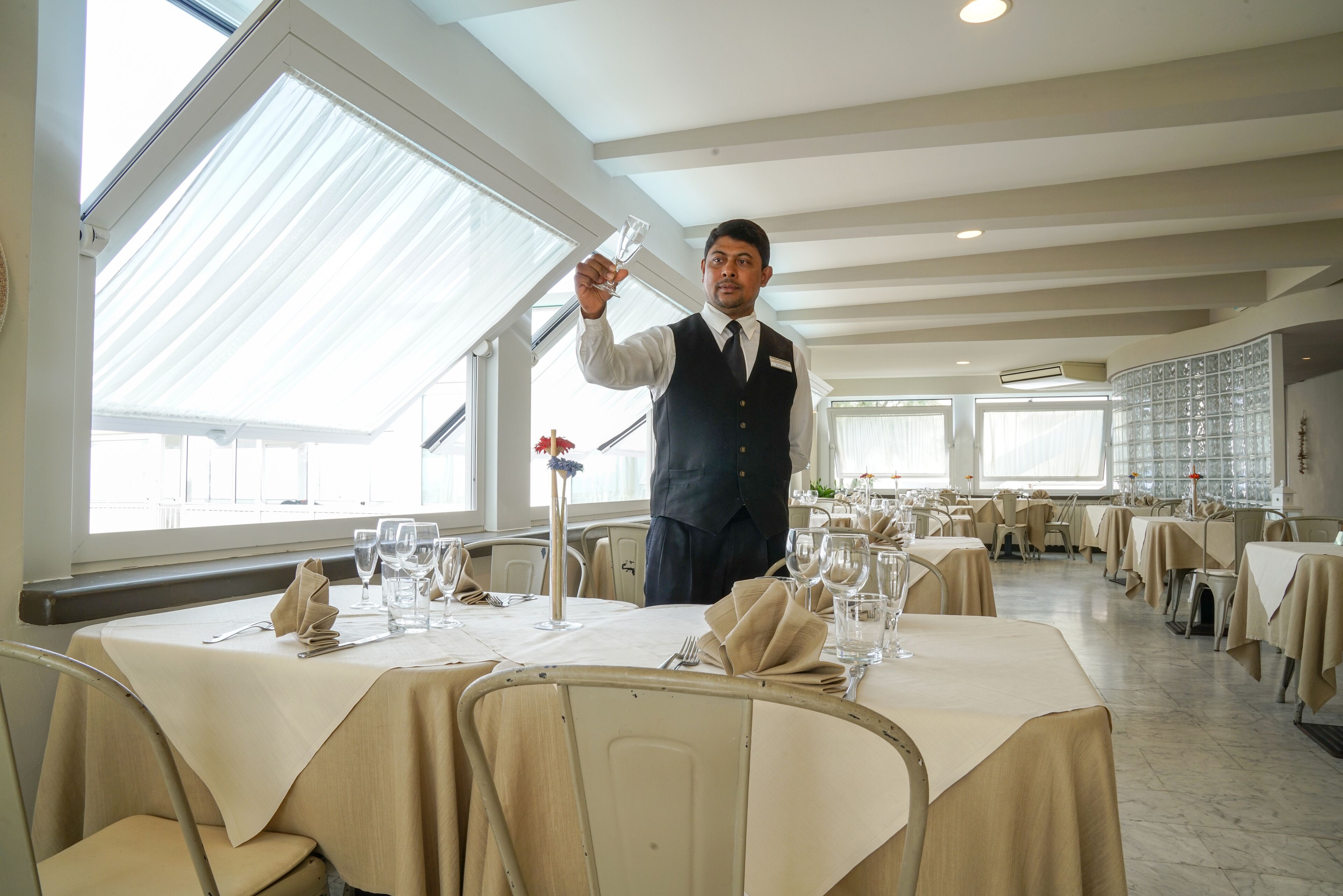 Un comedor bien iluminado con mesas dispuestas para el servicio, ventanas amplias y un diseño de interiores moderno.