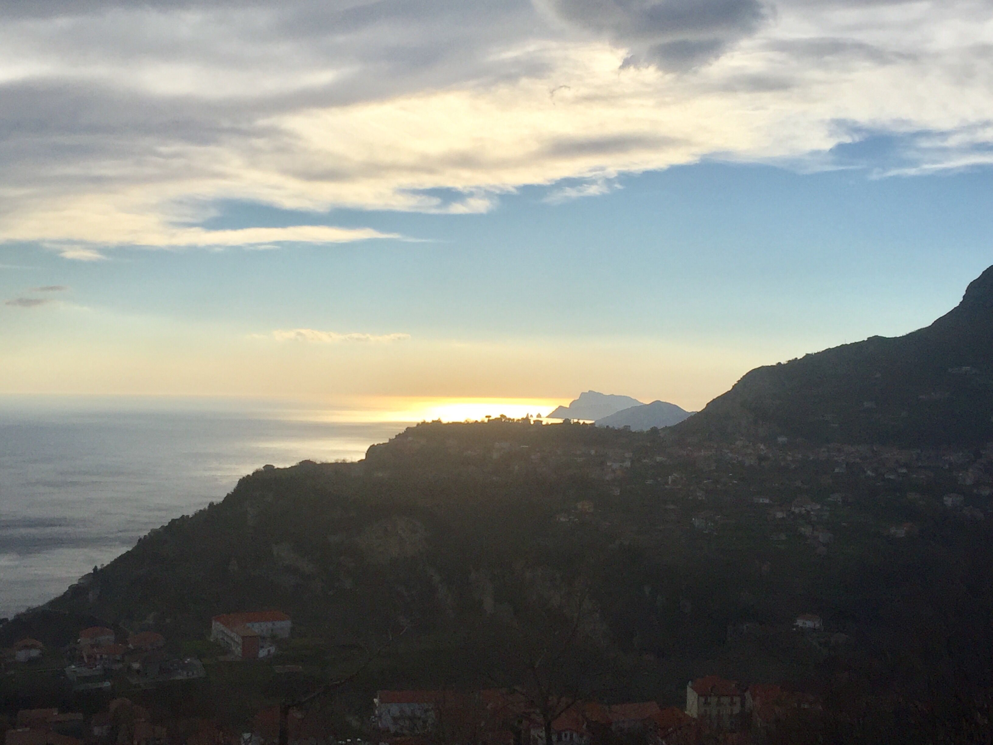A coastal landscape with a mountain in the background and a village in the foreground.