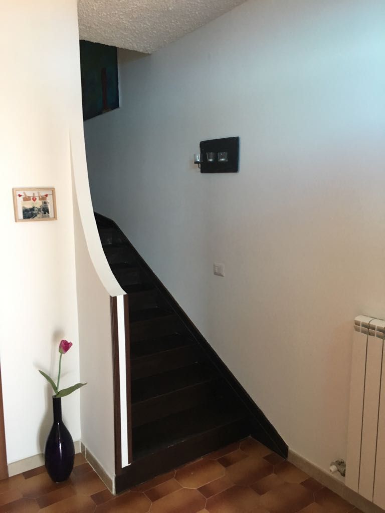 Una escalera con barandilla oscura y pared blanca con termostato.