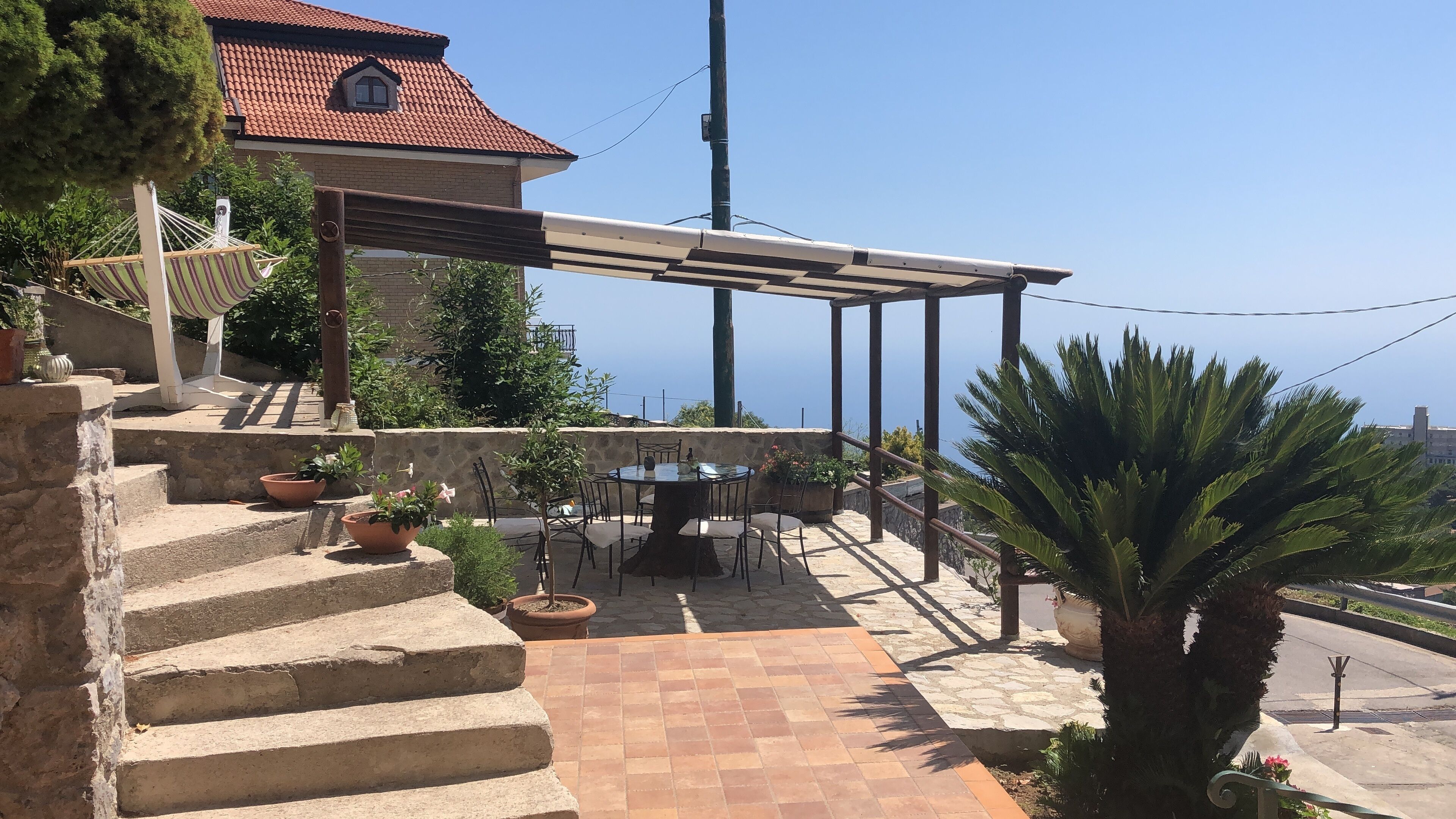 A patio with a table and chairs, surrounded by potted plants and a pergola.