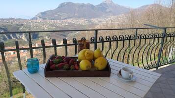 A table with a tray of strawberries and lemons, a blue jar, and a cup on a balcony with a mountain view.
