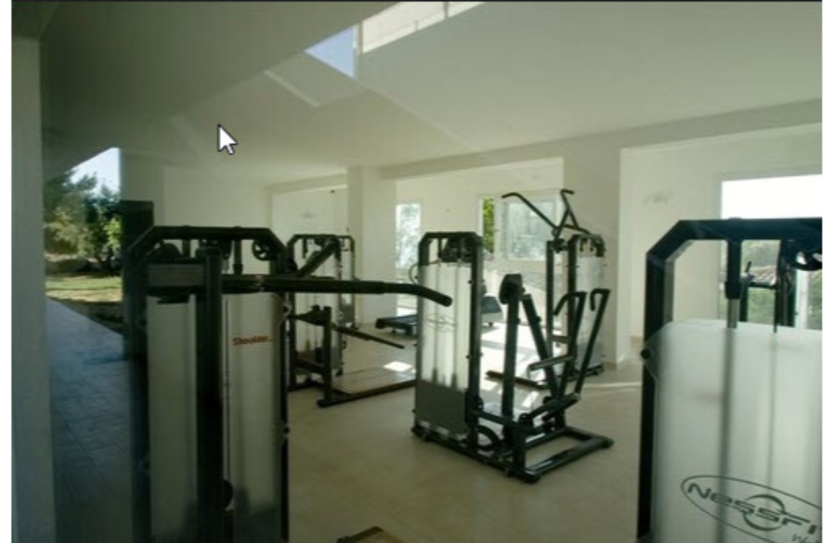 Ein Fitnessstudio mit verschiedenen Trainingsgeräten, großen Fenstern und einer Tür, die nach draußen führt.
