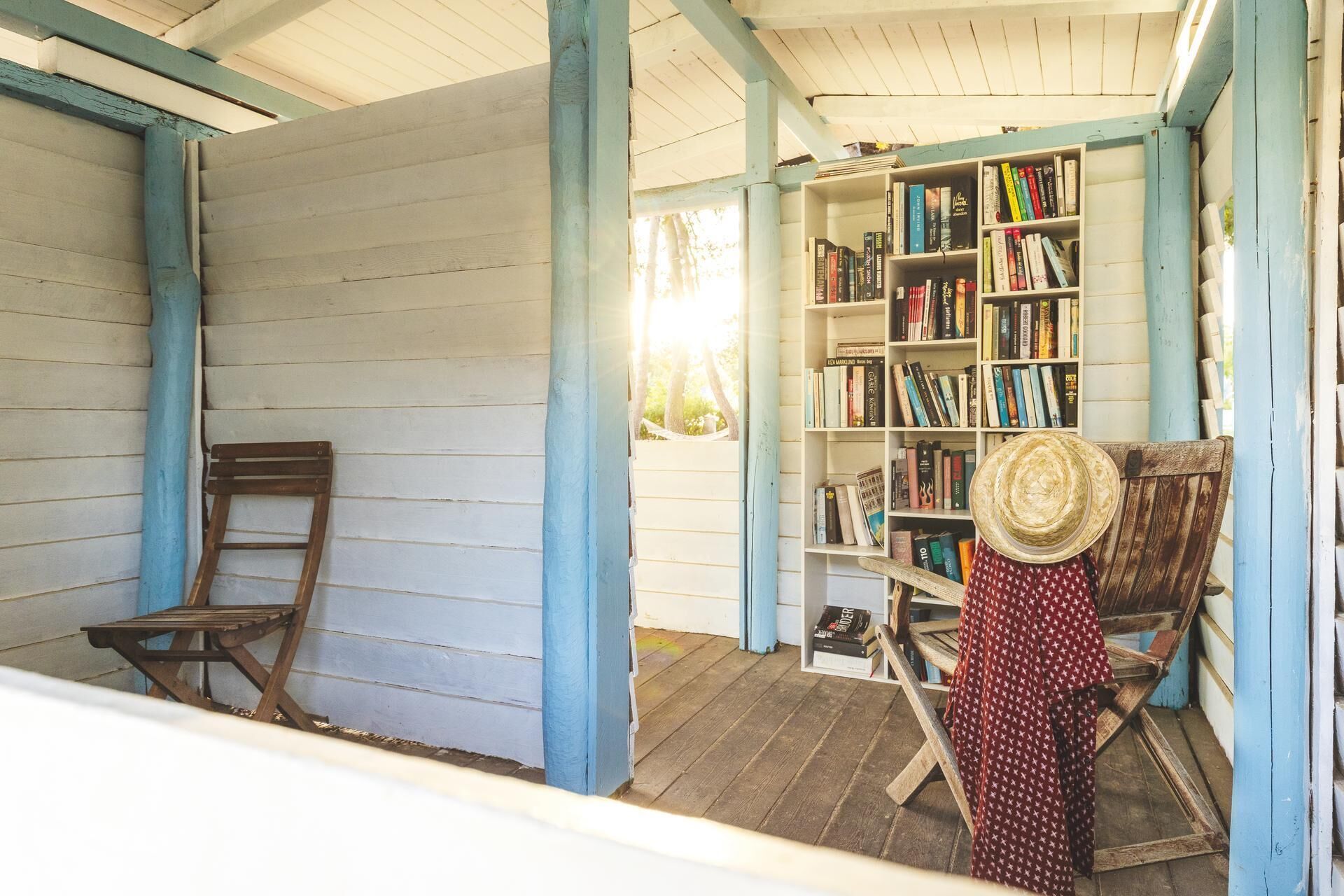 A wooden porch with a bookshelf, a wooden chair, and a hat.