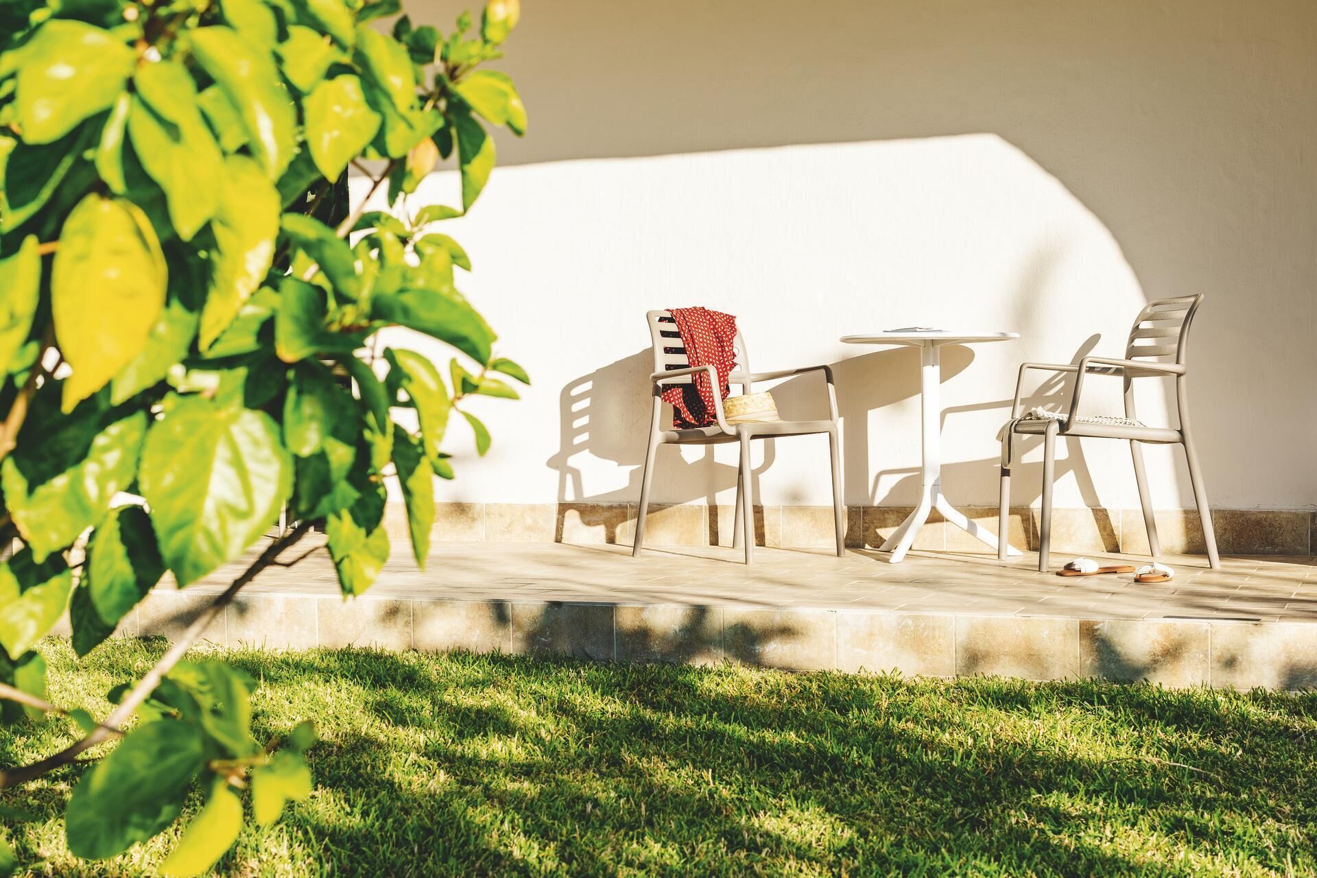 Een terras met een tafel, twee stoelen, een kleedje en een plant.