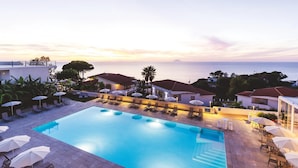 Piscina con sillones de descanso y sombrillas, con vista al mar.