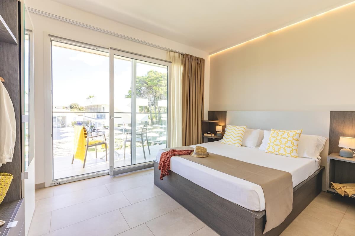A hotel room with a bed, a nightstand, a lamp, a window with curtains, and a view of the outside.