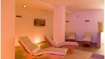 Ein Spa-Raum mit drei Liegen, einem wandmontierten Fernseher und einem kleinen Tisch mit einer Kerze.
