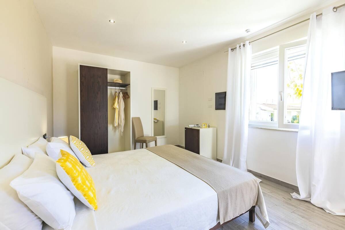 A bedroom with a bed, a chair, a wardrobe, a desk, and a window.