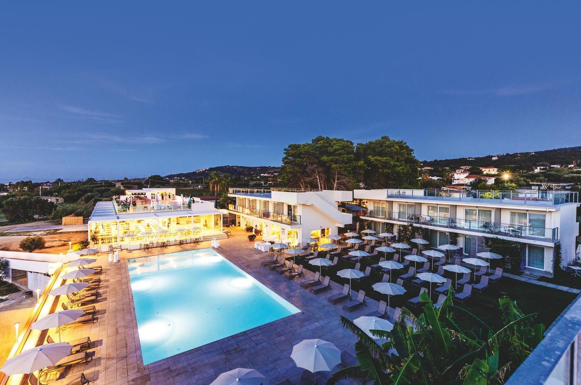 A rooftop pool area with lounge chairs and umbrellas, a swimming pool, and a view of the surrounding landscape.